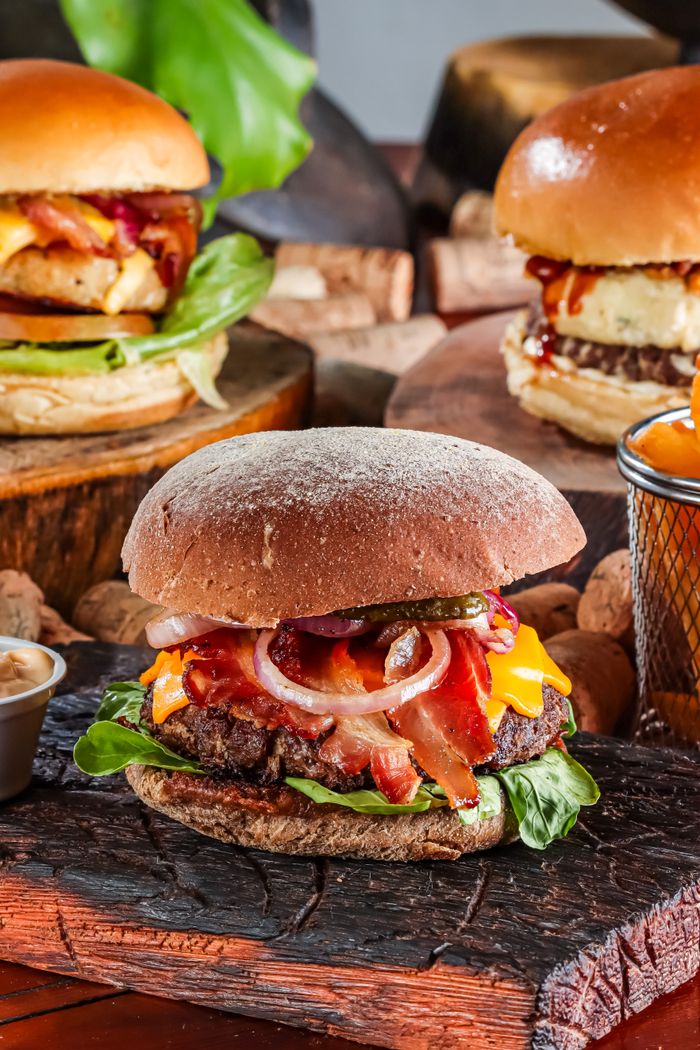 Close-up of gourmet burgers with cheddar, bacon, and vegetables on wooden boards.