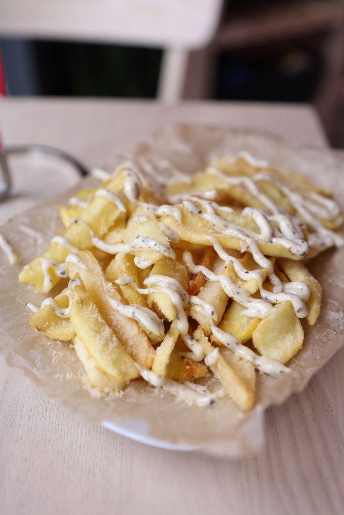 services-02 Crispy French fries drizzled with creamy sauce on a parchment-lined plate.