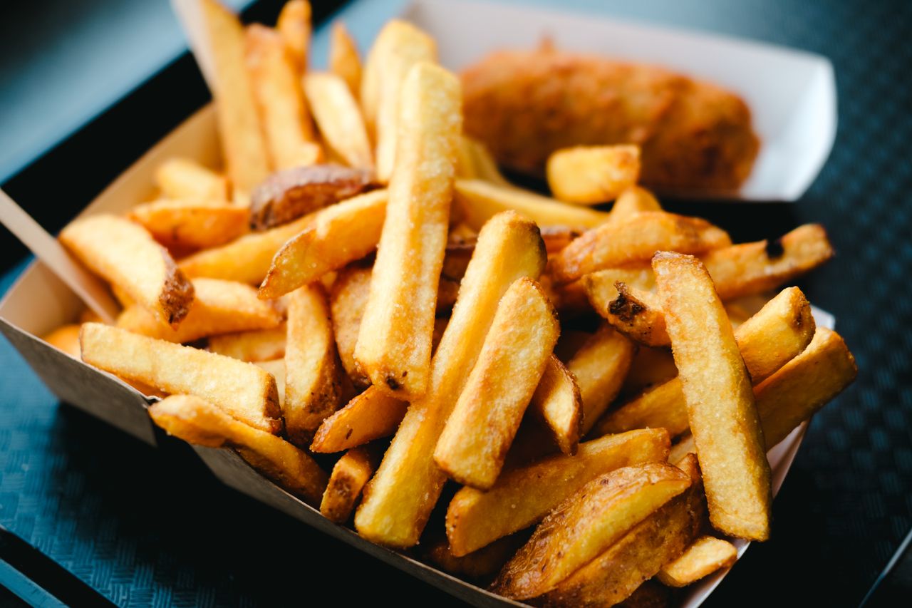 heros-img Close-up of delicious golden French fries in a paper box, served as a perfect snack or side dish.